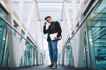 Young trainee standing in hall and carrying laptop with documents