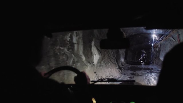 The car rides in a dark gloomy mine tunnel, illuminated by lanterns. View from inside the car, descends underground, into the mine.