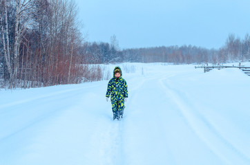 Cute Asian little child boy a green colorful jumpsuit  portrait  smiling on a  white fluffy snow in Siberia. Happy baby playing in the park outdoors in snow on cold winter day. With a smile of happy