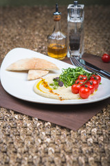 Traditional appetizer hummus with bread cakes, pita, on a plate with vegetables and sauce.
