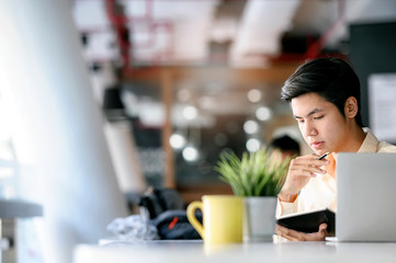 Portrait of young businessman working and thinking while sitting at office desk in modern office