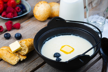 Traditional breakfast milk porridge with butter and berries on a wooden table.