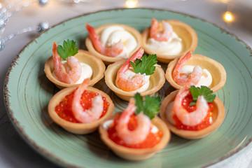 Tartlets with soft cheese, shrimp and red caviar. Holiday dish. On a green plate.