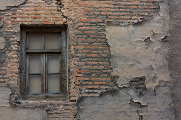 An aged wooden window in a weathered surface wall of an old bricked house.