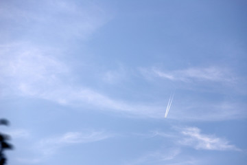 Airplane flying into the blue sky amid clouds and sunlight  Jet track on Blue saturated sky white clouds, bright sunny day.