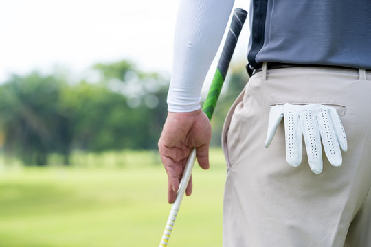 Croped shot of professional golf player carrying  golf gloves on his back and holding putter looking on green,