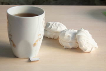 white marshmallow next to a mug of tea on a white table. lunch break.
