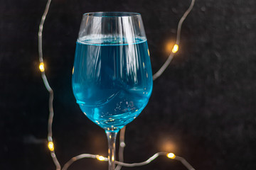 Blue wine in a glass on a dark background. In the background bokeh of lights. Festive mood.