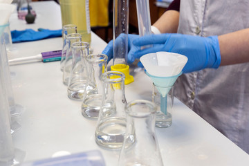 Hands of a worker in blue protective gloves performing chemical tests close-up. Chemistry of solutions. Modern science concept