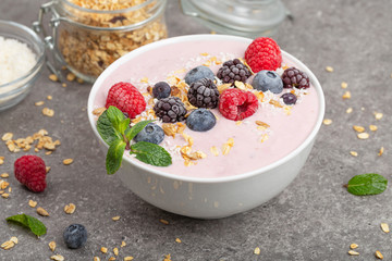 Berry smoothie bowl topped with blueberries, raspberry, blackberry, coconut flakes, yoghurt, muesli and mint for healthy breakfast, selective focus. Vegan food