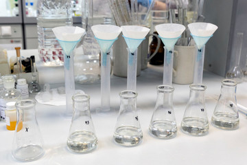 Long rows of glass flasks and cylinders with a clear liquid during a research experiment on a laboratory bench against the background of other equipment. The concept of modern science.
