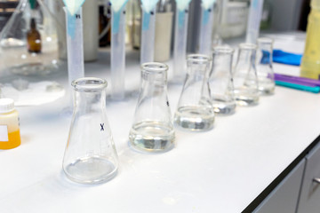 A long row of glass flasks with a clear liquid during a research experiment on a laboratory bench. The concept of modern science.
