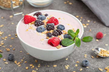 Berry smoothie bowl topped with blueberries, raspberry, blackberry, coconut flakes, yoghurt, muesli and mint for healthy breakfast, selective focus. Vegan food