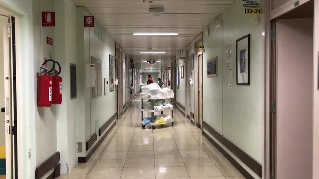 Long hospital corridor, medical personnel walking along it. Special patient transportation in clinic hallway, trolley with clean towels for patients. Hospital hallway concept