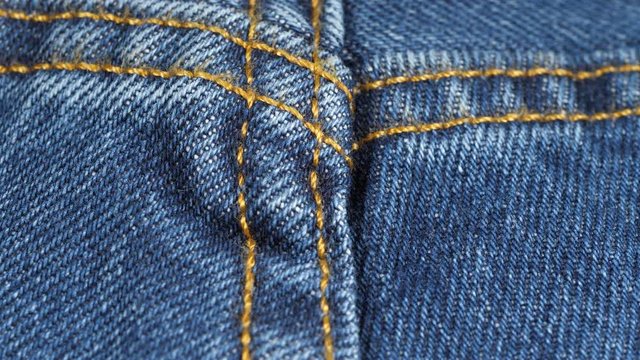 Seam on denim jeans, tracking macro. Denim textile texture, close up low angle. Dolly shot