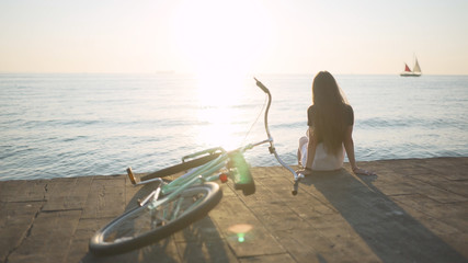 Young beautiful woman with a bicycle is having a good time at the sea at sunset or sunrise 