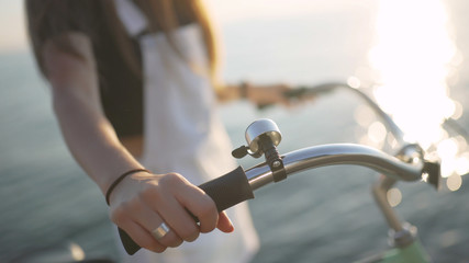 Young beautiful woman with a bicycle is having a good time at the sea at sunset or sunrise 