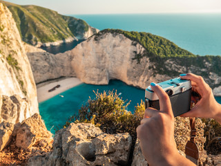 Young woman tourist taking pictures in Zante - Zakynthos, Greece. Shiprweck Beach at sunset