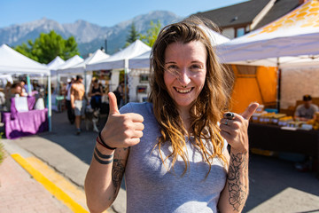 A healthy caucasian girl gives the thumbs up at local street fair for artisans and farmers, front...