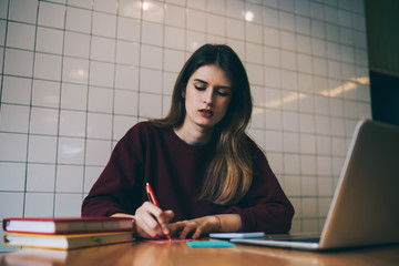 Young hipster girl freelancer with notepad at coworking space learning language by internet doing...