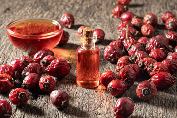 A bottle of rose hip seed oil with dried rose hips on a table