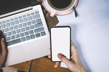 Close up top view of female hands holding smartphone with big screen front laptop keyboard working with documents at table. Sharing files via bluetooth between devices. Browsing network web via app