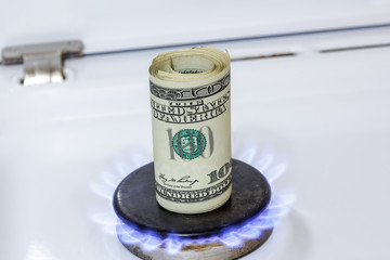 gas burner on which there is a roll of one hundred dollar bills. Symbol of rising fuel prices.
