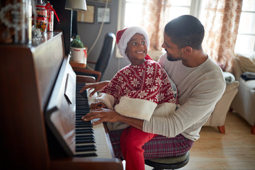 Happy Girl and father  together play music at piano on Christmas Day.