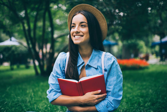 Happy Female Student In Stylish Hat Holding Textbook For Education And Laughing Enjoying Time For Literature Hobby, Positive Ukrainian Hipster Girl With Popular Best Seller Rejoicing Outdoors