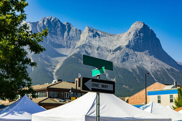 A wide angle view of a Canadian street scene, with tall mountains and blue sky behind market stalls...