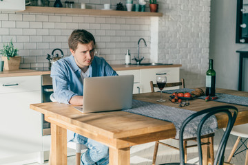 Young man drinking wine while working on laptop