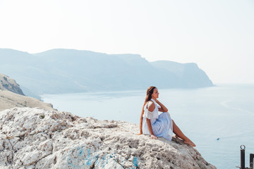 Beautiful woman with long hair in dress on cliff landscape in a journey