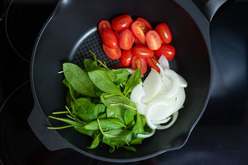 cherry tomatoes, spinach and onions in a pan. Stages of cooking vegetarian pasta. Vegetarianism concept