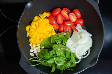 cherry tomatoes, spinach, onions, garlic and sweet peppers in a pan. Stages of cooking vegetarian pasta. Vegetarianism concept