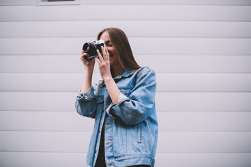 Young smiling female amateur photographer making pictures using vintage camera near wall outdoors , positive caucasian hipster girl trying taking photo with favorite retro equipment on free time