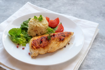 fried chicken breast fillet with cauliflower risotto, lettuce and tomato on a white plate and napkin, grey background with copy space