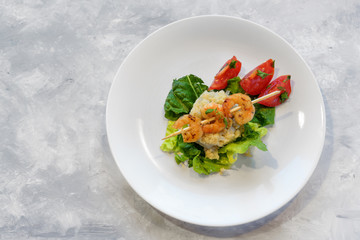 appetizer from shrimp skewers on a cauliflower risotto heap, lettuce and  tomatoes on a white plate, light gray background with copy space, high angel top view from above