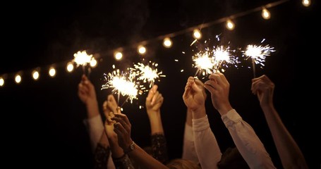 hands in the dark waving sparklers . on backdrop of garland. new year, holiday, Christmas, birthday, party. Cheerful Partying With Sparkler Fire Smiling . Night Shot - Powered by Adobe