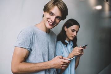 Smiling hipster guy looking away and laughing from received funny email with publication content, happy young male and female bloggers enjoying networking for socialising in virtual cell world