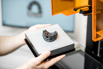 Dental technician removing jaw model from a 3d printer at the laboratory, modeling frame for implant production