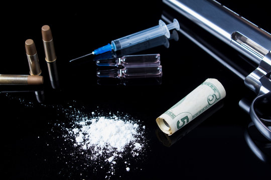 Drugs with a syringe, a gun and ammunition on a black mirror background. Dangerous bad habits, addiction to drugs and gambling. Crime because of drugs.