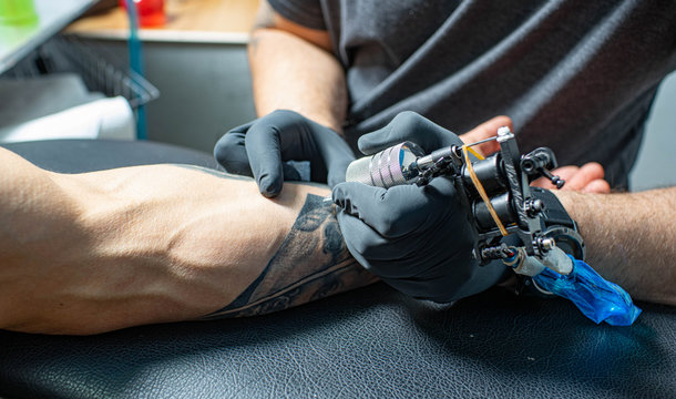 Male arm with tattoo. Master in black gloves is preparing to draw new tattoo. Tattoo machine.
