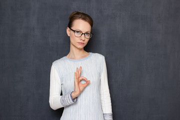 Portrait of serious focused woman with glasses, showing ok gesture