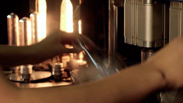 Woman working on harmful production plastic bottles from preforms, hands closeup. Puts blanks on molds of blowing machine on plant. Manufacture plastic utensils, manual labor, environment pollution.