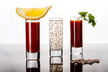 Three shots with tomato juice and chia drink on glossy table