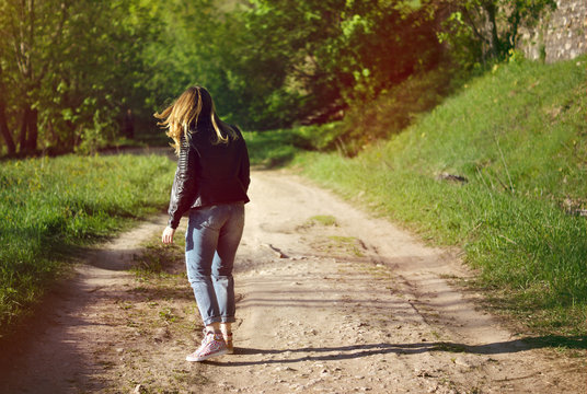 girl walking on the road to the forest looking towards the forest