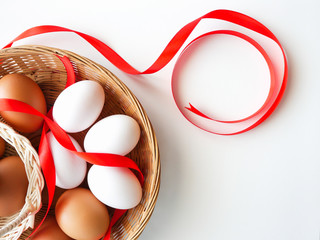 Healthy food concept, Gift set of fresh duck and chicken eggs in basket with red ribbon decorated on white table background-top view