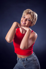 A portrait of smiling young woman with short blond hair in red shirt in front of black background. Lifestyle, emotions and beauty concept