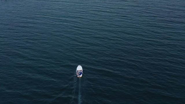 Aerial drone follows small white boat across expanse of open water