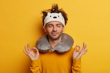 Relaxed passenger meditates indoor, tries to have rest during traveling in transport, wears neck...